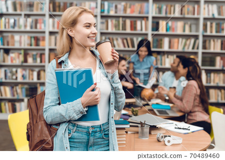 Young girl drinks coffee while standing in library Young girl drinks coffee while standing in library 70489460