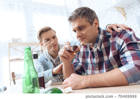 Father drinks alcoholic while son sits nearby. 70489998