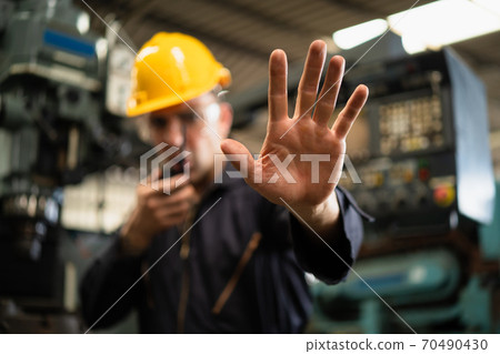 Selective focus of industrial worker in factory site gesture keep out while communicating with a walkie talkie, concept restricts access in industrial factory, working profession, factory restriction Selective focus of industrial worker in factory site gesture keep out while communicating with a walkie talkie, concept restricts access in industrial factory, working profession, factory restriction 70490430