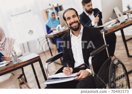 A man sits in a wheelchair and makes notes.  70491573