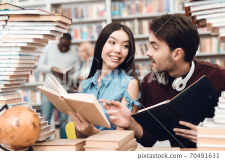 A girl looks at a guy while reading a book. A girl looks at a guy while reading a book. 70491631