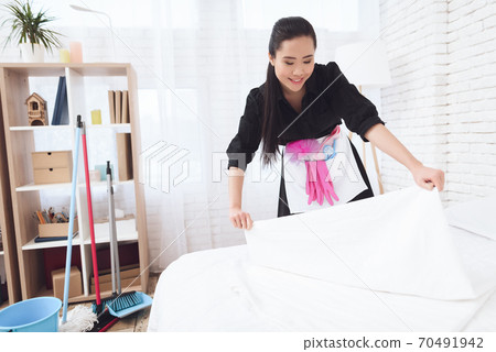 Asian woman in overalls makes a bed and cleans up. Asian woman in overalls makes a bed and cleans up. 70491942