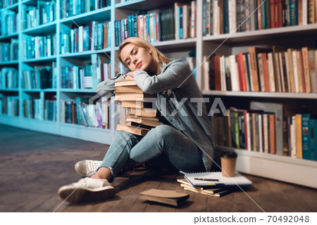 Girl sitting on the floor near a large shelf. 70492048