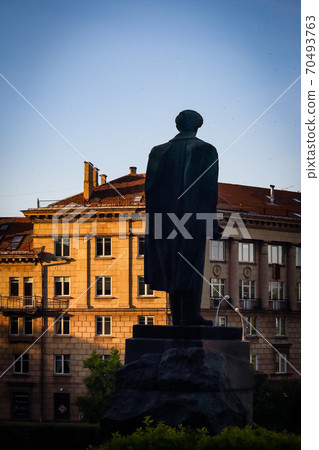 Big man's monument from behind silhouette standing on city square in sunset sun visible on a building wall Big man's monument from behind silhouette standing on city square in sunset sun visible on a building wall 70493763