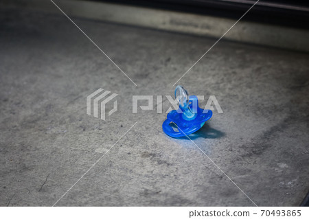 Blue kids pacifier dummy left on concrete surface 70493865
