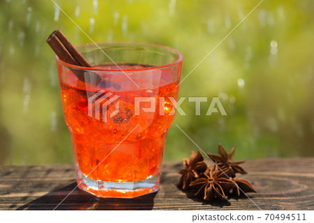 in a glass of colored soda water and a stick of cinnamon, against a background of greenery, drops of water 70494511
