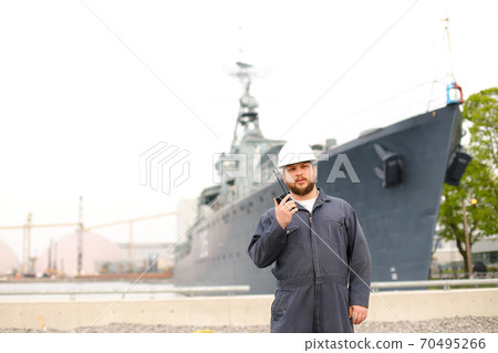 Marine deck officer talking by walkie talkie radio and standing near offshore vessel in bakground. 70495266