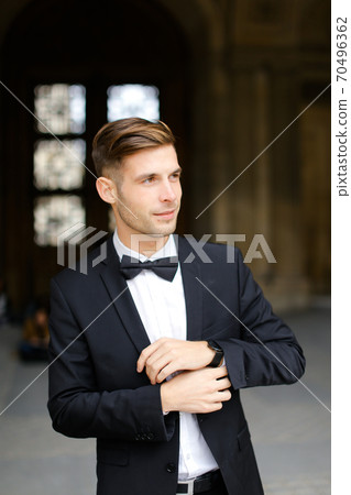 Young man standing and posing, wearing black suit and bow tie. Young man standing and posing, wearing black suit and bow tie. 70496362