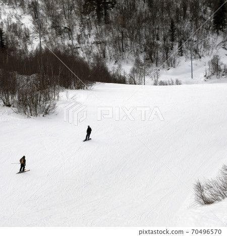 Skier and snowboarder downhill on ski slope at gray winter day Skier and snowboarder downhill on ski slope at gray winter day 70496570
