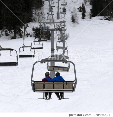 Two skiers on chair-lift in gray day Two skiers on chair-lift in gray day 70496625