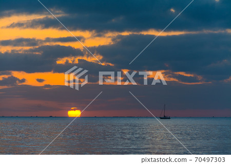 Boat sailing at sunset under a dramatic sky 70497303