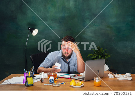 Ill young man with fever and cold looks suffering at home Ill young man with fever and cold looks suffering at home 70500181