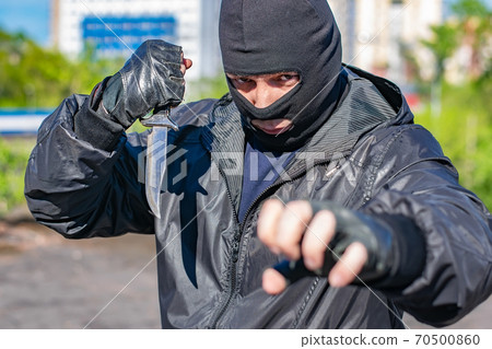 black masked bandit with a knife in his hand stands in a fighting stance black masked bandit with a knife in his hand stands in a fighting stance 70500860