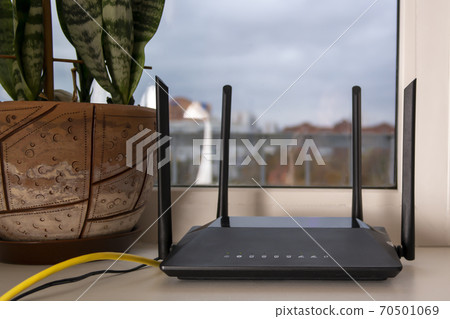 a black Wi-Fi router stands on the windowsill,next to a potted flower a black Wi-Fi router stands on the windowsill,next to a potted flower 70501069