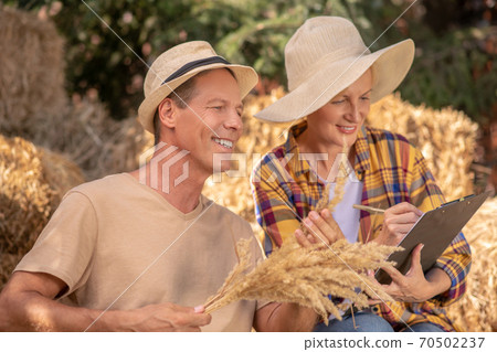 Female farmer taking notes, male sitting next to her with bunch of millet spikelets Female farmer taking notes, male sitting next to her with bunch of millet spikelets 70502237