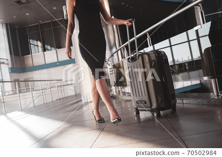 Woman carrying a suitcase through the airport Woman carrying a suitcase through the airport 70502984