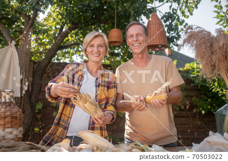Happy middle-aged couple shucking corn in the garden, smiling 70503022