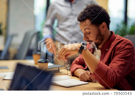 Business problems. Young frustrated and sad mixed race man sitting at desk and working in the modern office Business problems. Young frustrated and sad mixed race man sitting at desk and working in the modern office 70503543