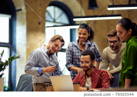 Group of happy multiracial business people looking at laptop screen, discussing project results and smiling while working together in the modern office or coworking space Group of happy multiracial business people looking at laptop screen, discussing project results and smiling while working together in the modern office or coworking space 70503544