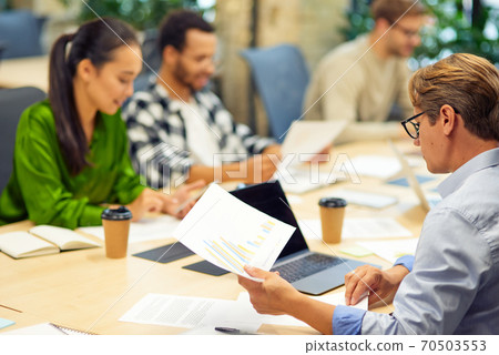 Brainstorming meeting. Group of multiracial people sitting at the desk in the modern coworking space or office and working on project together Brainstorming meeting. Group of multiracial people sitting at the desk in the modern coworking space or office and working on project together 70503553