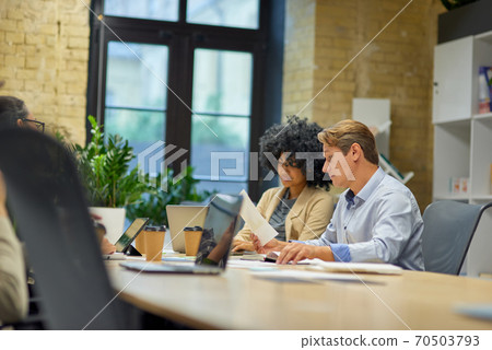 Two male and female coworkers looking at laptop screen and analyzing project results while sitting together at the table in the modern office or coworking space Two male and female coworkers looking at laptop screen and analyzing project results while sitting together at the table in the modern office or coworking space 70503793