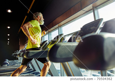Side view of a athletic middle aged man in sportswear running on a treadmill in a gym, doing cardio before workout 70504362