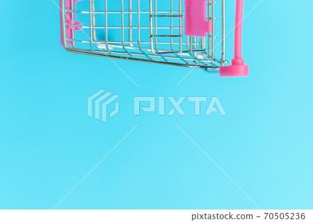 Small supermarket grocery push cart for shopping toy with wheels isolated on blue pastel colorful trendy background Copy space. Sale buy mall market shop consumer concept. 70505236