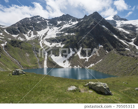 Beautiful turquoise blue mountain lake Grunausee in alpine landscape with green meadow and snow-capped mountain peaks. Tyrol, Stubai Alps, Austria, summer sunny day 70505313