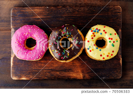 Glazed donuts with sprinkles on wooden board Glazed donuts with sprinkles on wooden board 70506383