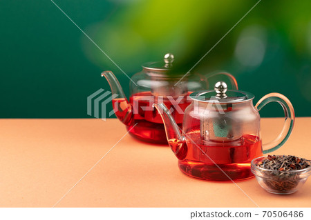 Glass teapot with black tea on background of blurred foliage 70506486