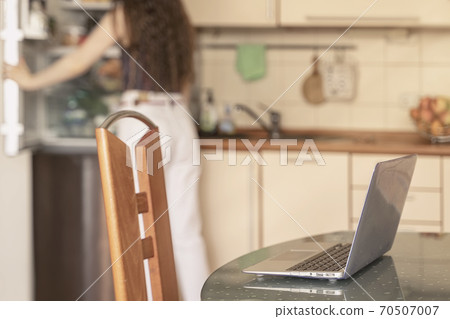 Notebook on the table of kitchen at home, lunch break, unrecognizable girl takes food from the refrigerator. Concept of remote work, home office. 70507007