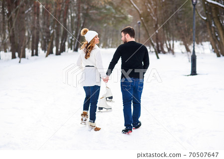 Close up loving couple walking on a date in a winter Park. Young man and his girlfriend holds each other to the hands and holding ice skates. Close up loving couple walking on a date in a winter Park. Young man and his girlfriend holds each other to the hands and holding ice skates. 70507647