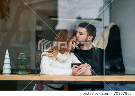 Dating in a cafe. Beautiful smiling girl with her boyfriend sitting in a cafe enjoying in coffee and conversation. 70507992