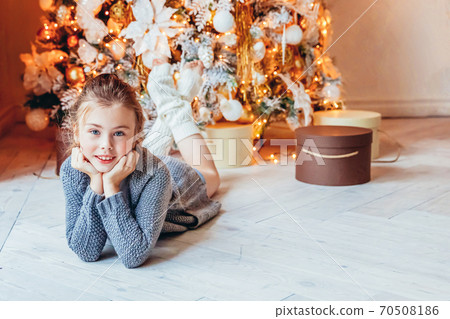 Little girl with gift box near Christmas tree on Christmas eve at home. Young kid in light bedroom with winter decoration Happy family at home Christmas New Year december time for celebration concept 70508186