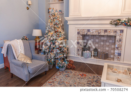 Classic Christmas decorated interior room, New year tree with silver decorations. Modern blue classical style interior design apartment with fireplace and armchair. Christmas eve at home. Classic Christmas decorated interior room, New year tree with silver decorations. Modern blue classical style interior design apartment with fireplace and armchair. Christmas eve at home. 70508274