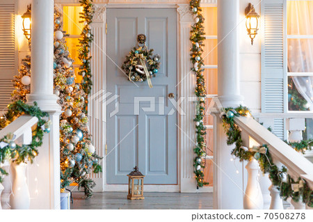 Christmas porch decoration idea. House entrance decorated for holidays. Golden and green wreath garland of fir tree branches and lights on railing. Christmas eve at home 70508278