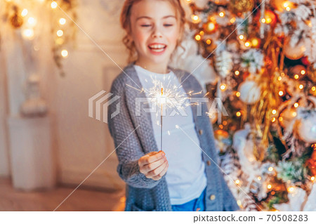 Little girl with sparkler near Christmas tree on Christmas eve at home. Young kid in light bedroom with winter decoration Happy family at home Christmas New Year december time for celebration concept Little girl with sparkler near Christmas tree on Christmas eve at home. Young kid in light bedroom with winter decoration Happy family at home Christmas New Year december time for celebration concept 70508283