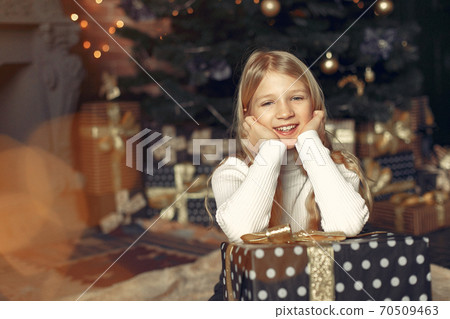 Little girl in a white sweater near christmas tree with present Little girl in a white sweater near christmas tree with present 70509463