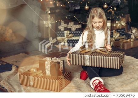 Little girl in a white sweater near christmas tree with present Little girl in a white sweater near christmas tree with present 70509470