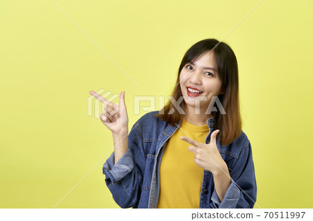 Young Asian woman pointing hands on yellow background Young Asian woman pointing hands on yellow background 70511997