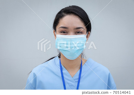 Portrait of female health worker wearing face mask against grey background 70514041