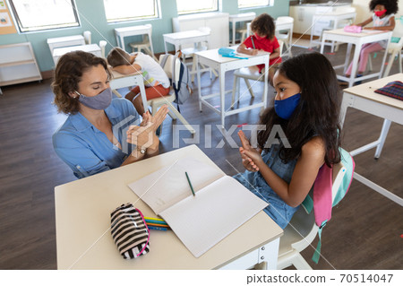 Female teacher and girl wearing face masks talking to each other through sign language in class Female teacher and girl wearing face masks talking to each other through sign language in class 70514047
