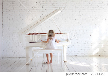 Girl in white dress playing piano in white hall with briks wall Girl in white dress playing piano in white hall with briks wall 70514358