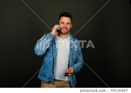 Handsome young man in a smart casual wear holding smart phone and looking at camera with smile 70516407