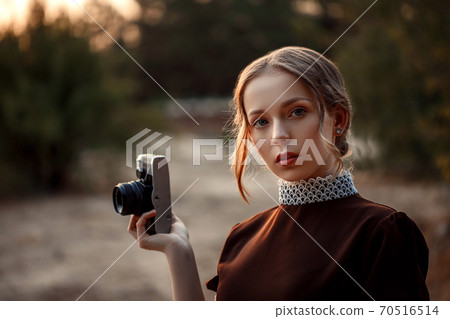 close-up portrait of a young beautiful girl in a brown dress in a retro style with a vintage camera in her hands on an abandoned road close-up portrait of a young beautiful girl in a brown dress in a retro style with a vintage camera in her hands on an abandoned road 70516514