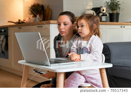 Mother and child girl sitting at home ad watching school video on laptop. Distant education Mother and child girl sitting at home ad watching school video on laptop. Distant education 70517345