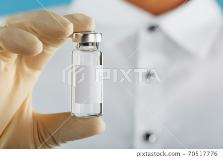 Ampoule in the hands of a researcher doctor in rubber gloves with a vaccine close-up and free space for text on the ampoule sticker. Ampoule in the hands of a researcher doctor in rubber gloves with a vaccine close-up and free space for text on the ampoule sticker. 70517776