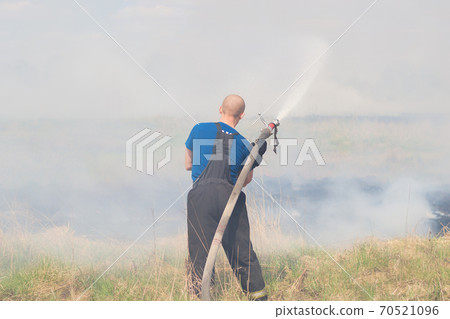 Firefighting on the field. Firefighter with a truck and a fire hose extinguishes fire.wildfire. Firefighting on the field. Firefighter with a truck and a fire hose extinguishes fire.wildfire. 70521096