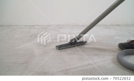 A worker is cleaning the concrete floor with a vacuum cleaner. A worker is cleaning a public concrete floor with a vacuum cleaner. Workers wear uniforms and use a blower to clean the floor. The master 70522652