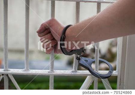closeup of hand being handcuffed to iron bars	 70524860
